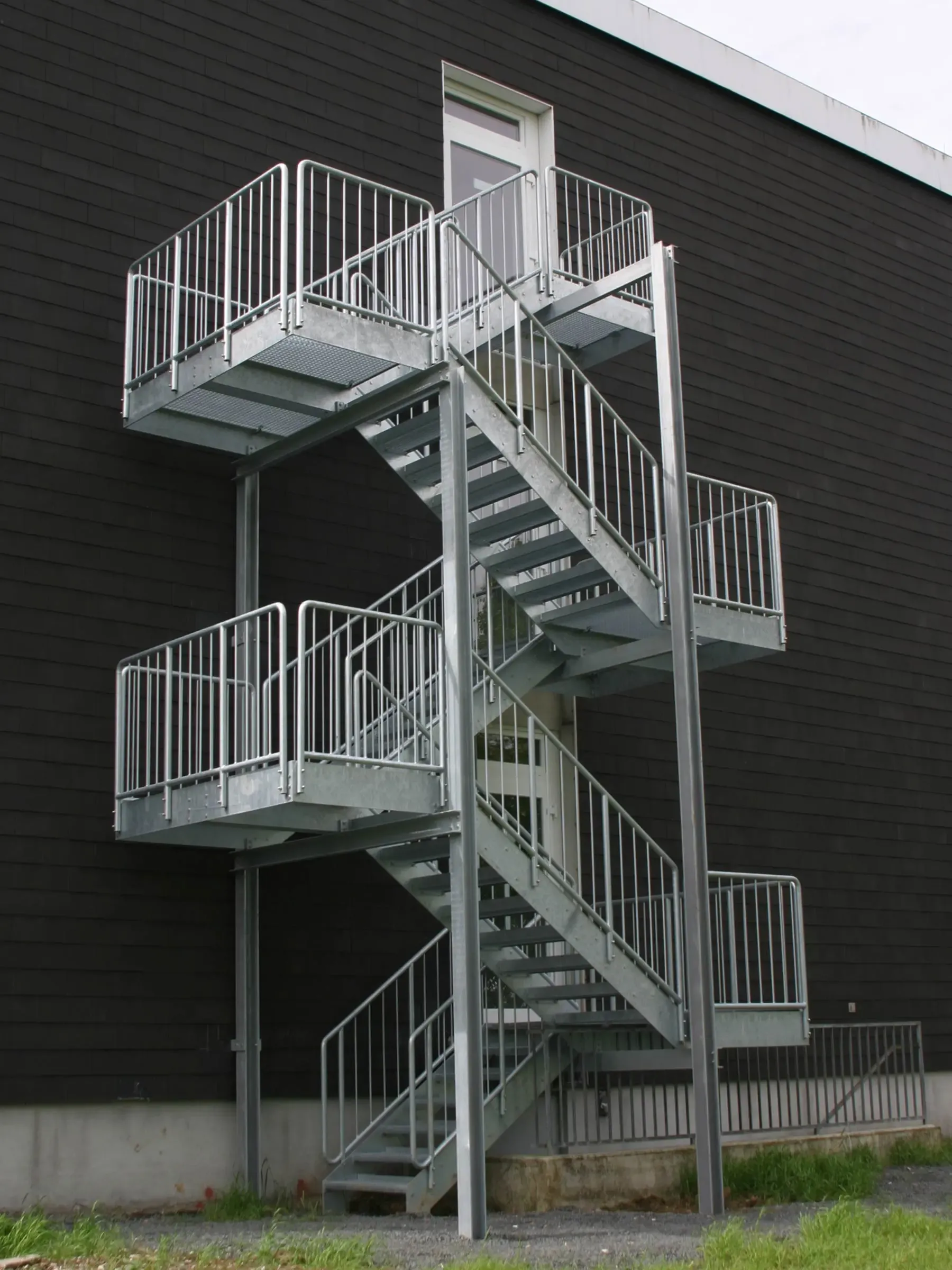 Verzinkte Stahltreppe als Fluchttreppe – mehrläufiger Treppenturm mit Geländer und Podesten, Außentreppe aus feuerverzinktem Stahl